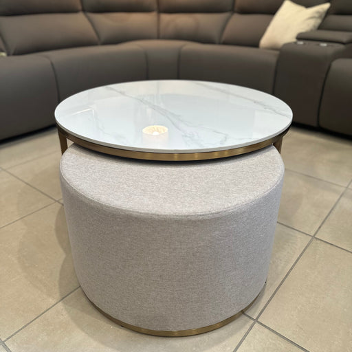 The Vienna Coffee Table + Footstool features a marble top with gold accents and a light gray upholstered ottoman beneath, placed in front of a modern dark gray sectional on tiled floors.