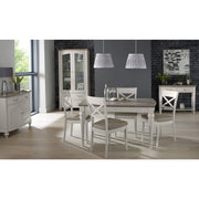 A modern dining room featuring the Montreux Dining Table in grey washed oak, upholstered chairs, two pendant lamps, a white cabinet, sideboard, large windows with natural light, dark walls, plus plants and art accents.