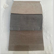 Three rectangular fabric swatches in beige, gray, and brown are stacked vertically on a white textured surface. With slightly frayed edges, these fabrics are ideal for upholstering the Westbury Storage Bedframe.