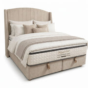 The Westbury Storage Bedframe is a plush beige lift-up bed with a tall, curved winged headboard, dressed in white and beige bedding, multiple pillows, and a patterned mattress labeled Regal Earl Contemporary Sleep.
