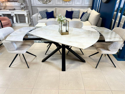 Modern dining room set featuring the Positano Table with a glass and sintered stone top, black metal base, and six Orbit upholstered chairs. A rectangular glass vase with white flowers and gold accents completes the look.