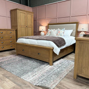 A cozy bedroom featuring the Aylesbury bedframe with matching wardrobe, dressers, and bedside tables. White bedding, floral pillows, a gray throw, two lamps, pink paneled walls, and a textured rug complete the inviting space.