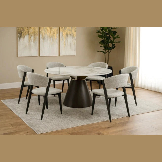 The Fusion 150cm Round Table with a dark base is paired with 6 Titan Chairs on a light gray rug. Wooden floors, a large plant, beige walls, and abstract gold artwork enhance this bright, contemporary dining space.