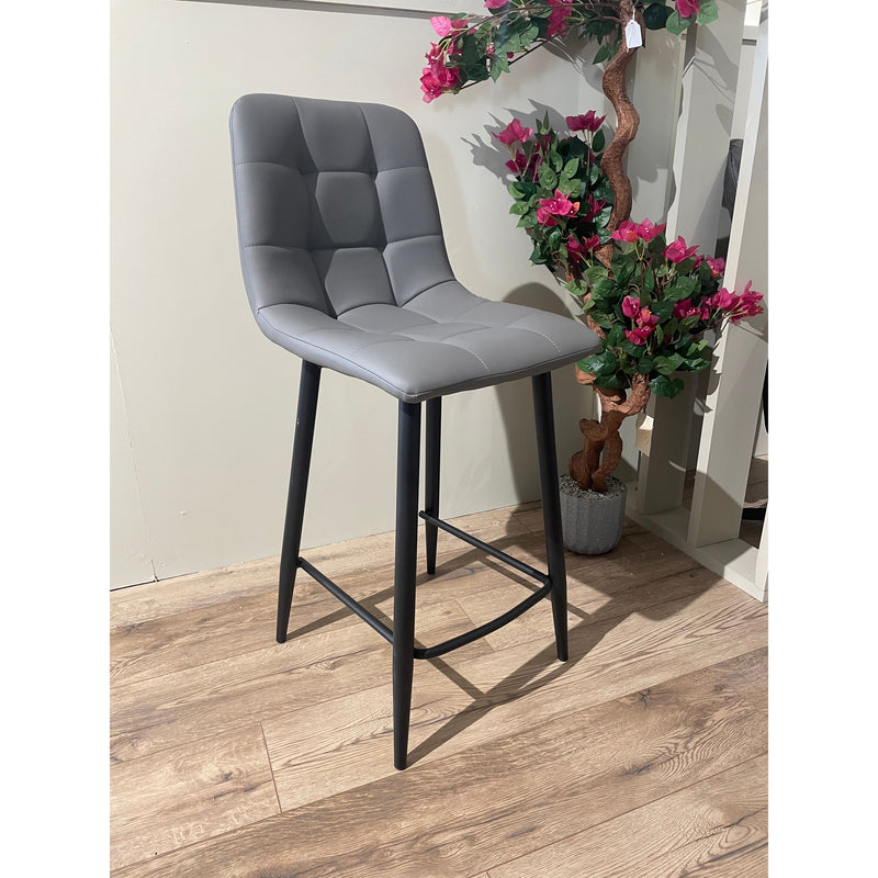 A black steel bar stool with a leatherette seat in gray, standing in a room with a potted plant and wooden flooring.