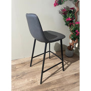 The Retro barstool features a dark gray seat and black metal legs, placed on a wood floor beside a potted plant with green leaves and pink flowers, bringing style to any light-colored space. Also available in multiple colour options.