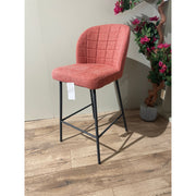 A red upholstered bar stool with a black metal frame and a cushioned top, standing on a wooden floor.