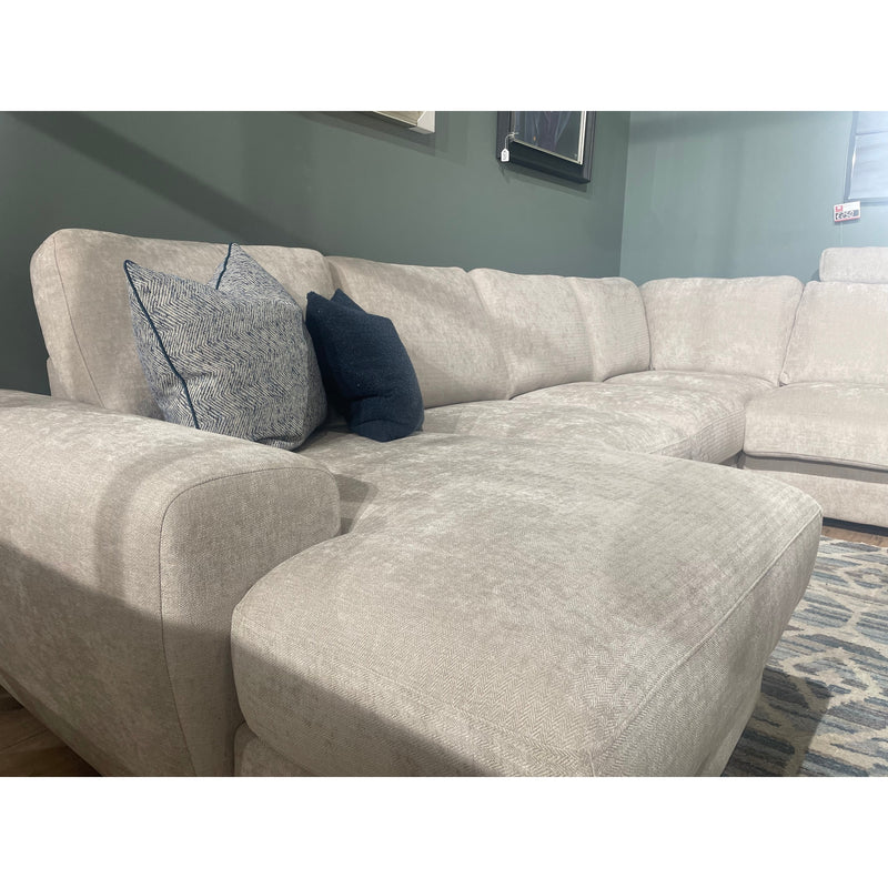 The Grand Corner Group 4L, a spacious light beige modular sofa with micro pocket springs and two blue accent pillows, is placed in a living room featuring green walls and a patterned rug.