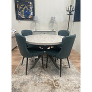 A round extending dining table with X-shaped legs and a light grey textured melamine top, displayed in a showroom setting.