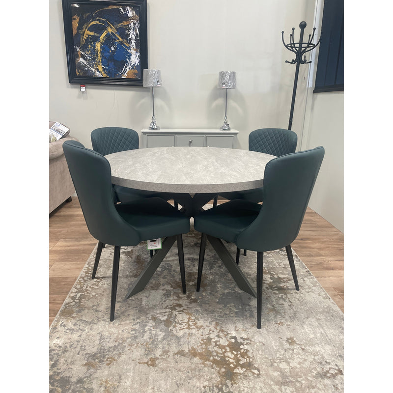 A round extending dining table with X-shaped legs and a light grey textured melamine top, displayed in a showroom setting.