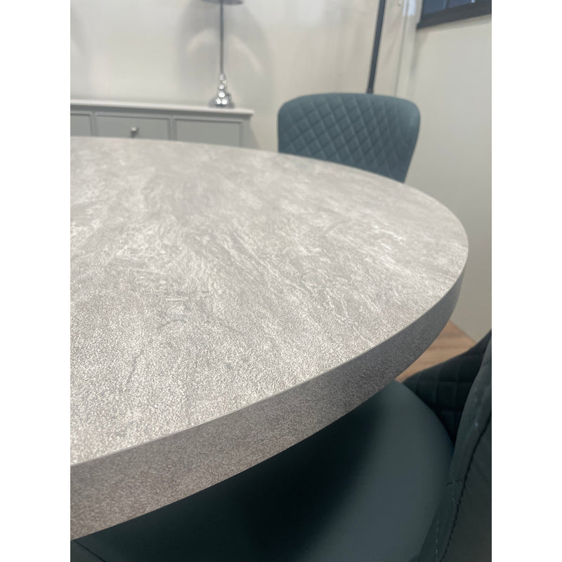 Detail shot highlighting the thick edge and textured finish of a contemporary round gray table, paired with an elegant dark green or teal dining chair.