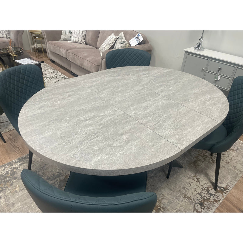 The Rimini Round Extending Table with a light gray stone-effect top is paired with four dark upholstered chairs, creating a space-saving setup on a patterned rug in a contemporary living room.