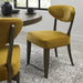 The Ellipse Fumed Oak Upholstered Chair with a quilted backrest and dark wooden legs sits beside a rustic oak dining table in a modern, light-filled room featuring a speckled area rug.
