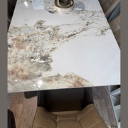 The Sorrento Dining Table, featuring a glossy marble effect with brown and beige patterns, is paired with beige upholstered seating and rests on a wooden floor, complete with a stylish round centerpiece.