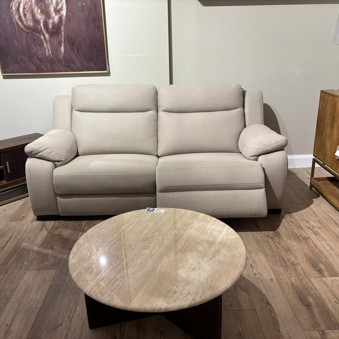 A Lorenzo Electric Recliner Sofa with padded arms and backrest sits against a light wall, paired with a round marble coffee table on a wooden floor. Wooden furniture and artwork complete the stylish setting.