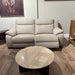 A Lorenzo Electric Recliner Sofa with padded arms and backrest sits against a light wall, paired with a round marble coffee table on a wooden floor. Wooden furniture and artwork complete the stylish setting.