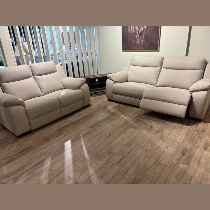 Two Lorenzo Electric Recliner Sofas in beige are arranged on a wooden floor in a stylish living room. One sofa’s footrest is extended, vertical blinds cover the window, and a painting hangs behind the sofas.