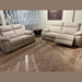 Two Lorenzo Electric Recliner Sofas in beige are showcased on a wooden floor in a showroom, with vertical blinds covering the window and a painting displayed above.