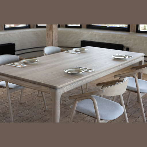 The Floating Dining Table, custom crafted from ash wood with six matching chairs, is set and ready. Brick floors, wooden beams, and wall windows enhance the inviting atmosphere of the dining space.