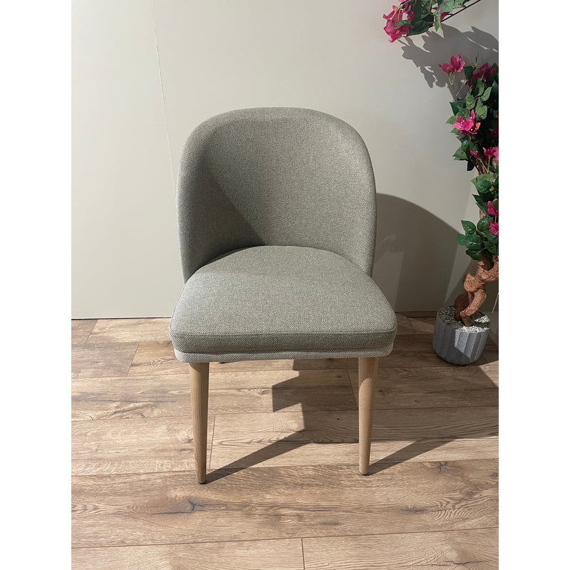 Contemporary accent chair with smooth, rounded lines and light oatmeal or tweed fabric, set on a wood floor.