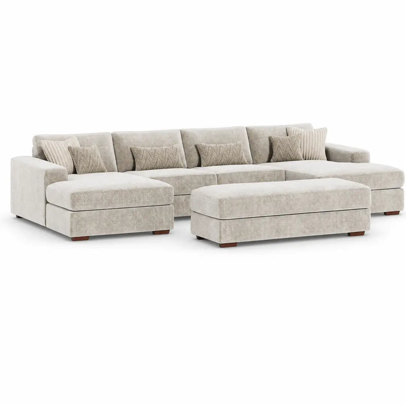 The Henley Sofa is a beige sectional with a left-facing chaise, matching ottoman, and five back cushions. It comes with four decorative pillows featuring chevron patterns. This contemporary sofa showcases low wooden legs and a plush, modern design, all upholstered in soft chenille fabric for enhanced comfort and style.