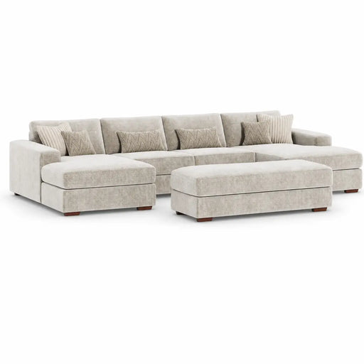 The Henley is a spacious, light beige modular sofa with a matching ottoman, upholstered in soft chenille and accented by patterned throw pillows, displayed against a plain white background.