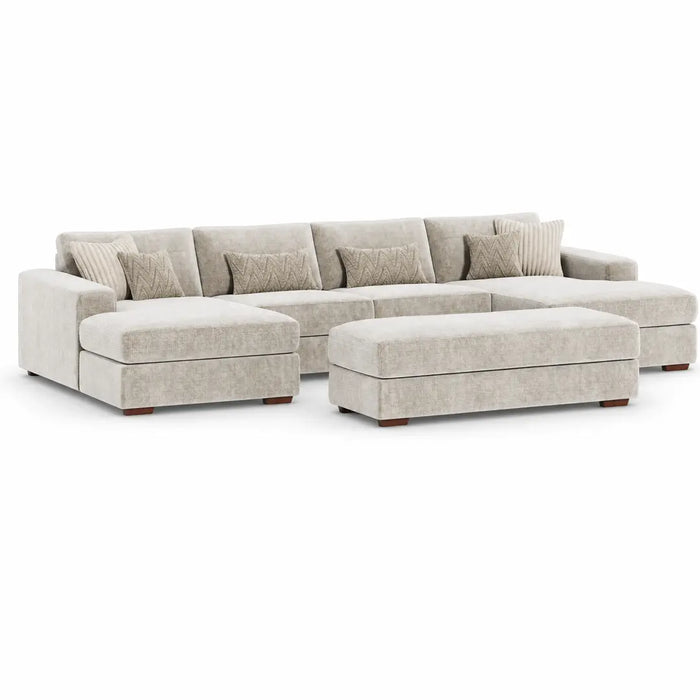 The Henley is a spacious, light beige modular sofa with a matching ottoman, upholstered in soft chenille and accented by patterned throw pillows, displayed against a plain white background.