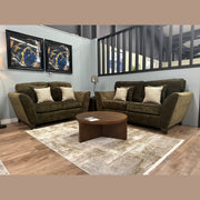 Two comfortable Cosmos Sofas with beige accent pillows face each other in a modern living room, divided by a round wooden coffee table on a light rug. Two abstract artworks hang above one sofa on the light blue wall.