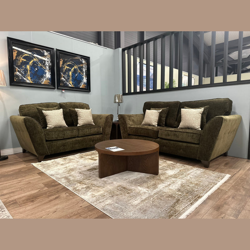 Two comfortable Cosmos Sofas with beige accent pillows face each other in a modern living room, divided by a round wooden coffee table on a light rug. Two abstract artworks hang above one sofa on the light blue wall.