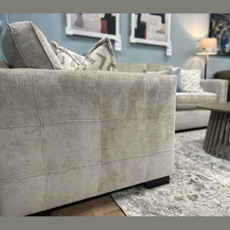 Close-up of the Ivy Corner Sofa in light gray premium fabric with patterned pillows, paired with a round wooden coffee table, a rug, and abstract art on the wall in a cozy living room.