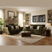A cozy living room features the Cosmos Sofa, a dark green seat, wooden coffee table, neutral decor, large windows, stone fireplace, houseplants, abstract art—all atop a light area rug and wooden floor.