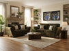 A cozy living room features the Cosmos Sofa, a dark green seat, wooden coffee table, neutral decor, large windows, stone fireplace, houseplants, abstract art—all atop a light area rug and wooden floor.
