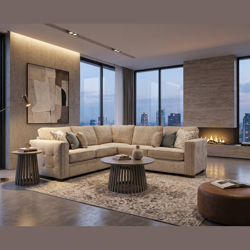 A modern living room features the Ivy Corner Sofa in beige with a contemporary silhouette, a round coffee table, side tables, abstract wall art, floor lamp, fireplace, and floor-to-ceiling windows overlooking a city skyline at dusk.