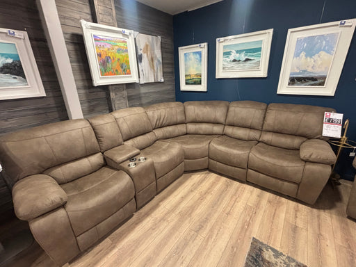 The Sapphire Corner Group, a spacious brown reclining sofa with cup holders, is displayed in a showroom with blue and wood-paneled walls, wooden flooring, and colorful landscape and seascape paintings above.