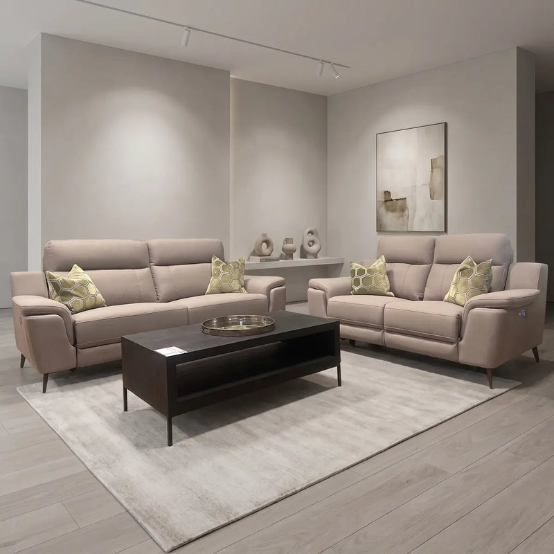 Modern living room featuring the Chloe Electric Recliner and a second beige piece, green patterned throw pillows, a dark wood coffee table, a light rug, minimalist decor, and abstract art on a neutral-toned wall.