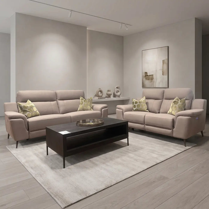 A modern living room featuring the Chloe 3+2 Electric Recliner Sofa with beige seating, green and cream geometric pillows, a dark wood coffee table with a tray, a light area rug, minimalist decor, and neutral-toned abstract wall art.