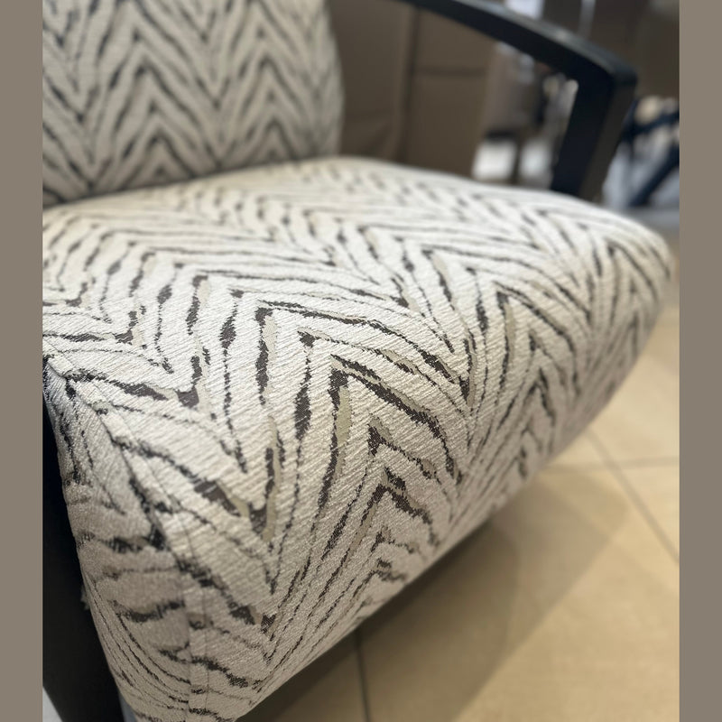A close-up of the Falcon Accent Chair featuring a white and black zigzag patterned fabric, sleek black armrests, and set against a beige tiled floor background.