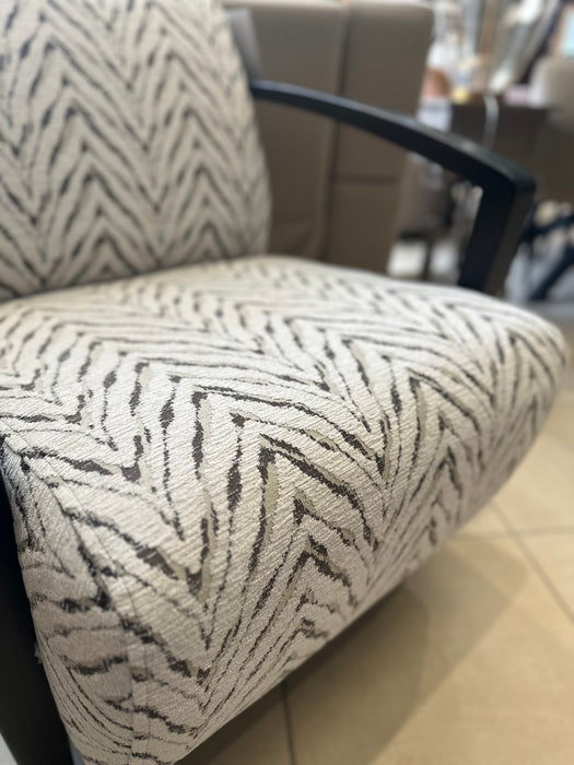 A close-up of the Falcon Accent Chair featuring a white and black zigzag patterned fabric, sleek black armrests, and set against a beige tiled floor background.