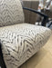 A close-up of the Falcon Accent Chair featuring a white and black zigzag patterned fabric, sleek black armrests, and set against a beige tiled floor background.