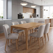 Modern kitchen with grey cabinets, wood accents, and a wooden dining table surrounded by six Mia Dining Chairs featuring taupe leather upholstery and solid oak legs on wooden floors under two round pendant lights.