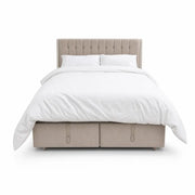 The Bella Ottoman Bed, featuring beige upholstery, a tall tufted headboard, and ample storage, is pictured with white bedding—including pillows and a duvet—against a plain white background, making it a stylish addition to your bedroom furniture collection.