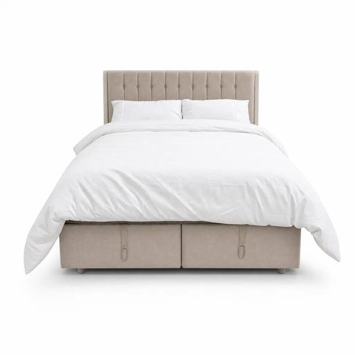 The Bella Ottoman Bed, featuring beige upholstery, a tall tufted headboard, and ample storage, is pictured with white bedding—including pillows and a duvet—against a plain white background, making it a stylish addition to your bedroom furniture collection.