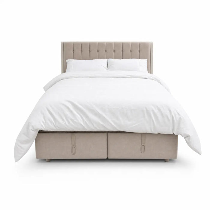 The Bella Ottoman Bed, featuring beige upholstery, a tall tufted headboard, and ample storage, is pictured with white bedding—including pillows and a duvet—against a plain white background, making it a stylish addition to your bedroom furniture collection.