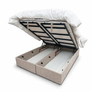The Bella Ottoman Bed features a beige upholstered design with a lifted mattress frame, revealing two spacious storage compartments underneath, set against a white background.
