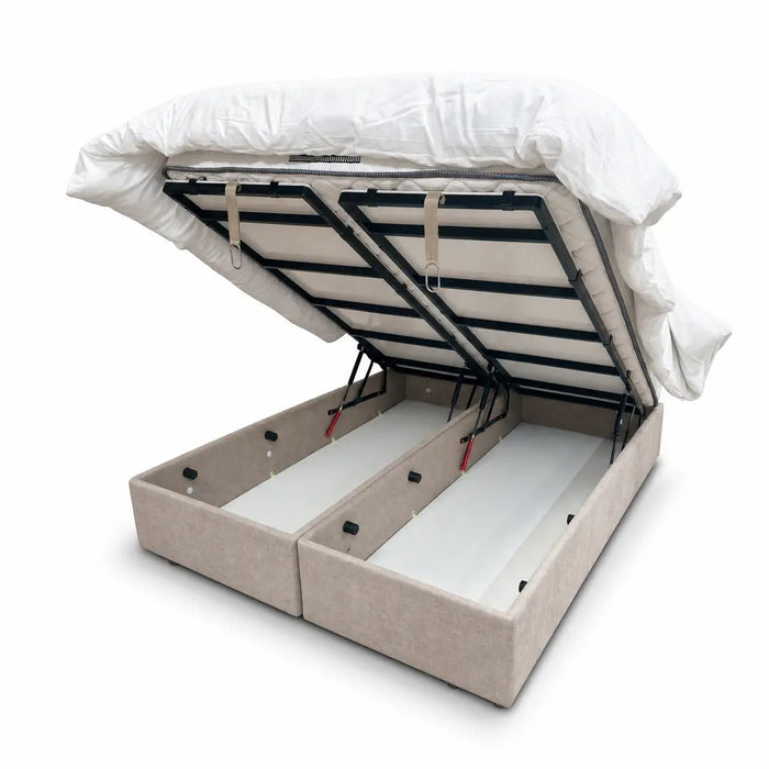 The Bella Ottoman Bed features a beige upholstered design with a lifted mattress frame, revealing two spacious storage compartments underneath, set against a white background.