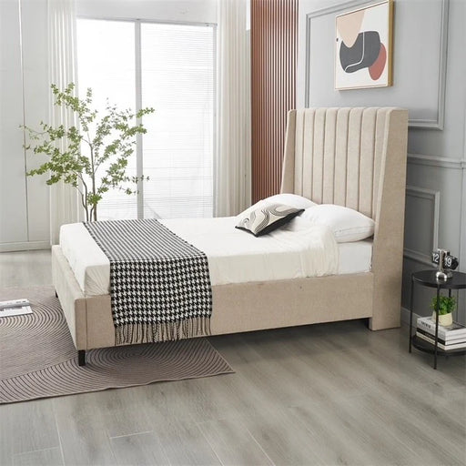 A modern bedroom with the Oscar Bedframe in beige, white bedding, and a black-and-white throw. A black side table holds a lamp and clock, a plant sits by the window, and abstract art decorates the wall.