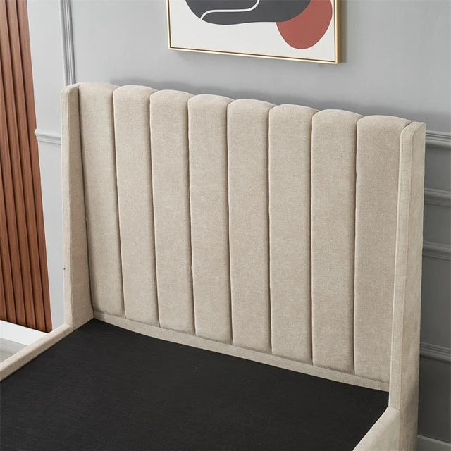 The Oscar Bedframe, a contemporary upholstered bed with a high, vertically tufted wingback design, is showcased in a minimal bedroom. A gray wall with decorative molding and an abstract artwork above the headboard complete the look.