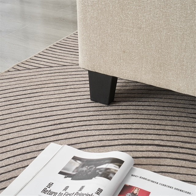 A close-up of a beige sofa leg on a light gray rug with dark stripes beside an open magazine—perfect inspiration for styling the Oscar Bedframe in your modern space.