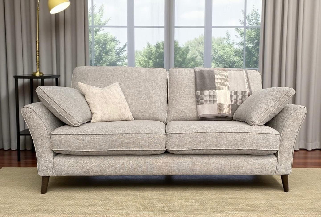 The Retro sofa features light gray Aquaclean fabric, beech frames, two cushions, and a plaid blanket on a beige rug. A floor lamp stands left of the sofa by large windows with gray curtains revealing green trees. Made to order.