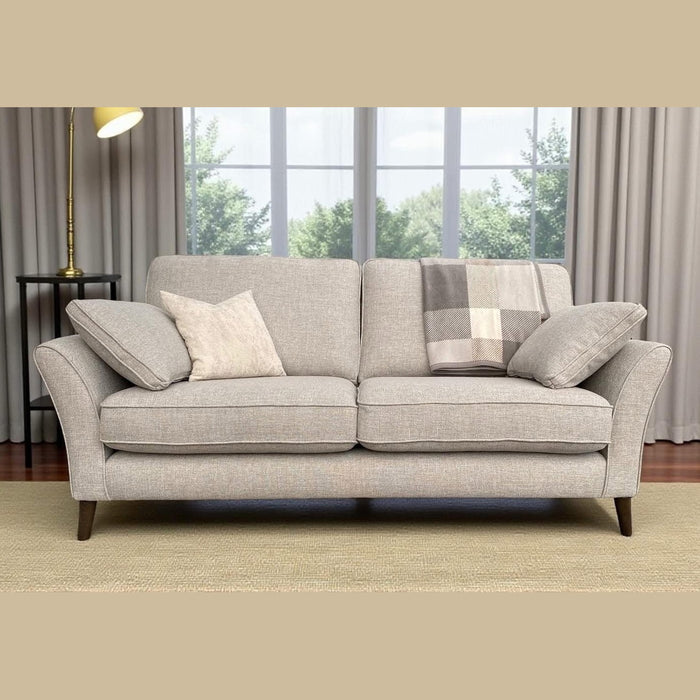 A Retro Sofa Range in light gray with angled arms and beech frame sits by a curtained window. Two cushions, a cream pillow, and a plaid blanket rest atop it. Wooden legs and a lamp nearby add to the cozy ambiance.