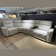 The Avery Electric Recliner Corner, a modern gray L-shaped sectional sofa with tufted backrests and a built-in armrest console in the corner, sits on display atop a mix of tile and wood flooring—making it an ideal centerpiece for any contemporary living room.
